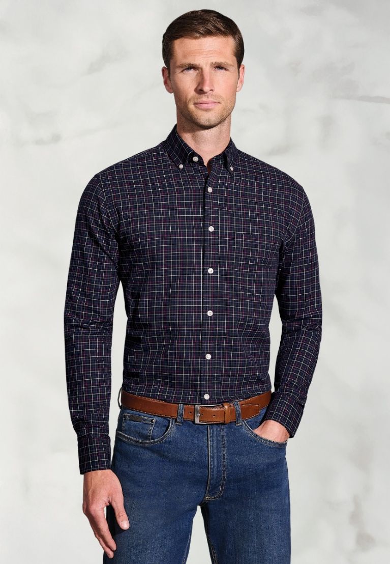 Man wearing a dark blue checkered shirt and jeans against a light gray background